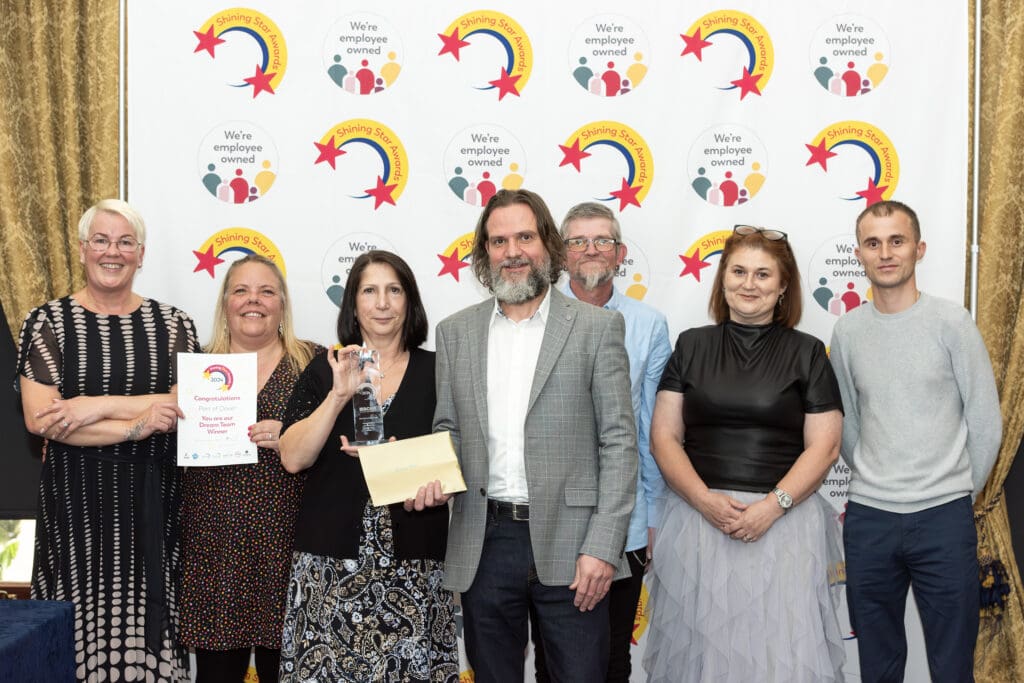 Team shot of people standing in front of a branded background holding a certificate and trophy 